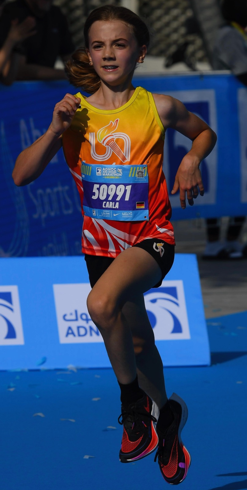 Carla running on the blue carpet of the Abu Dhabi Marathon, bib 50991