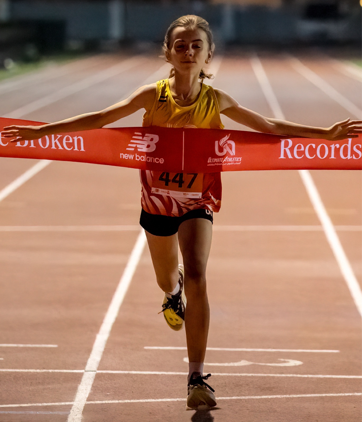 Carla breaking the finish tape on a track, bib 447