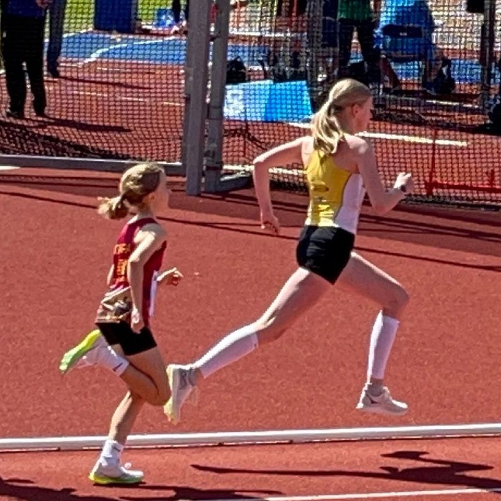 Two girls racing on a red track, Carla leading in a yellow vest
