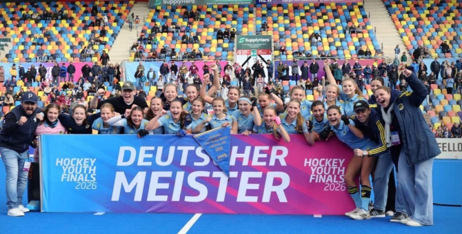 The Zehlendorfer Wespen girls' U16 celebrating behind a 'Deutscher Meister' banner in the Hockeypark stadium