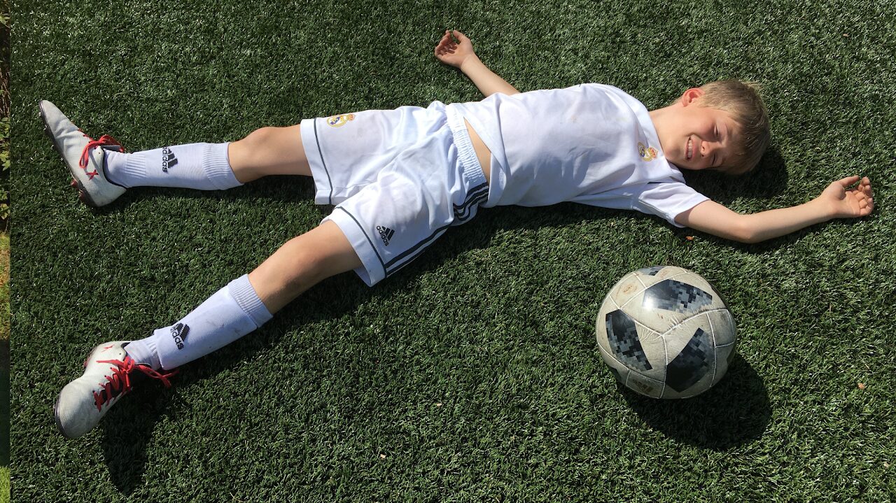 Young Max in a white Real Madrid kit lying on the pitch next to a ball